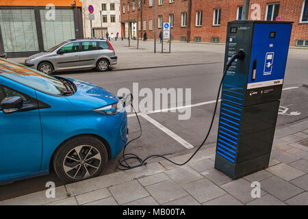 Elektrische Auto ist an der grünen Elektrizität Ladestation mit Ladekabel, München, Bayern, Deutschland Stockfoto