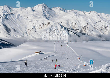 Skifahrer und Snowboarder auf den Grand Lac Piste über St Martin de Belleville auf einen klaren, sonnigen Morgen nach Neuschnee. Stockfoto