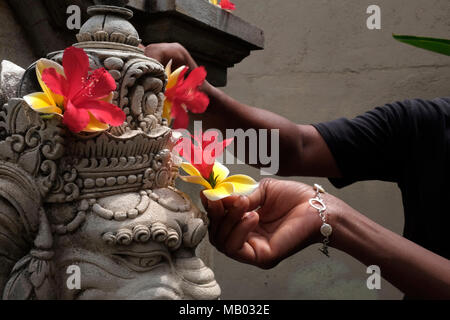 Die Arme von zwei Menschen, Blumen auf einem Ganesha Statue. Stockfoto