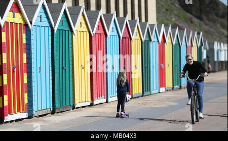 Menschen machen sich auf den Weg vorbei an bunten Badekabinen am Strand Boscombe in Bournemouth, Dorset. Stockfoto