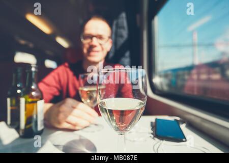 Transport auf der Schiene in sonniger Tag. Lächelnden jungen Mann Wein trinken Wein auf personenzug. Selektiver Fokus auf das Weinglas. Stockfoto