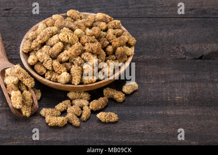 Nahaufnahme von getrocknete weiße Maulbeeren Früchte in eine hölzerne Schüssel und Löffel auf dunklem Hintergrund und leeren Raum für die Eingabe von Text Stockfoto