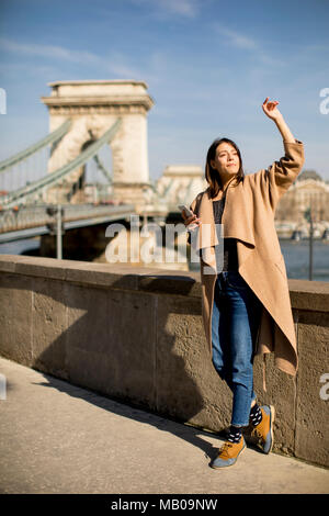 Junge Frau mit Mobiltelefon mit Chain Bridge im Hintergrund in Budapest, Ungarn Stockfoto