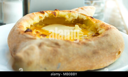 Ajarian oder Adjaruli Khachapuri, gefüllt mit Käse und garniert mit einem rohen Ei und Butter - traditionelles Gericht der georgischen Küche Stockfoto