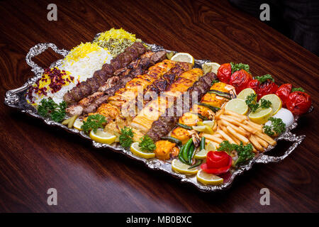 Volle Sicht auf den Persischen Mix Kebab von Hackfleisch und Hühnchen mit Reis und Pommes frites und Gemüse in einem großen traditionellen Fach auf hölzernen Tisch Stockfoto