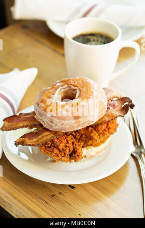 Hot würzigen gebratenes Huhn und Schinken Sandwich in einem Donut mit einer Tasse Kaffee Stockfoto