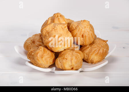 Windbeutel Windbeutel frische Kuchen und Gebäck Sahne in eine weiße Platte gefüllt auf weißem Holz- Hintergrund. Beliebte persischen Dessert Stockfoto