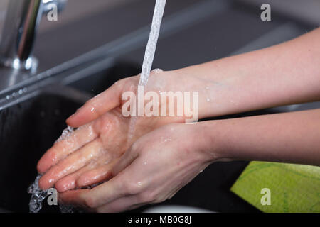 Junge Frau ihre Hände waschen in einem Spülbecken in der Küche halten sie unter fließendem Wasser aus dem Wasserhahn in der Nähe zu sehen. Stockfoto