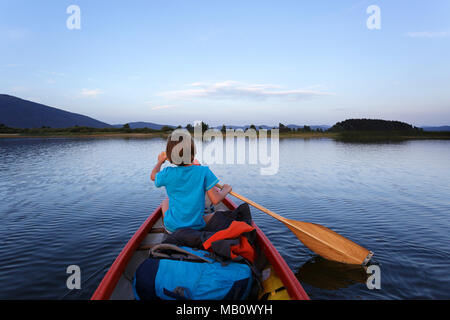 Junge Paddeln in einem Kanu auf einem See in der Dämmerung Stockfoto