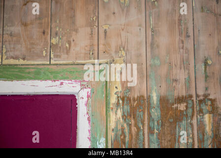 Detail einer alten Holzwand mit abblätternden Farbschichten in Grün, Rosa und weiß, die verwitterte Textur und rustikalen Charakter zeigen Stockfoto