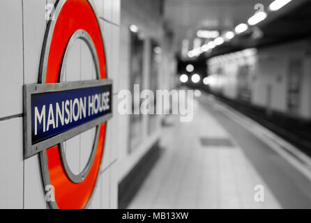 25. März 2018 - London, England. U-Bahnhof Mansion House roundel Zeichen auf der Plattform. Zug im Hintergrund. Stockfoto