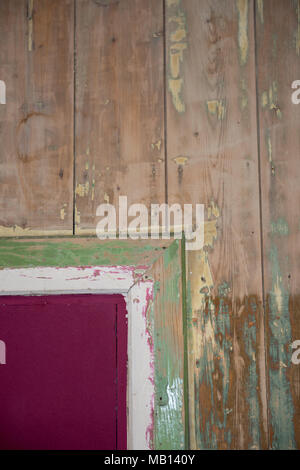Detail einer alten Holzwand mit abblätternden Farbschichten in Grün, Rosa und weiß, die verwitterte Textur und rustikalen Charakter zeigen Stockfoto