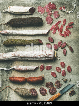 Vielzahl von spanischen oder italienischen Wurstwaren Würste. Flachbild-lay von fuets und salamies in Schichten über rauhe grauer Beton Hintergrund ausschneiden, Ansicht von oben Stockfoto