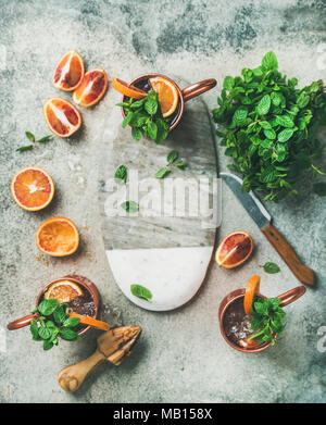 Blutorange Moscow Mule Alkohol Cocktails mit frischen Minzeblättchen und Eis in Kupfer Tassen und Board im Zentrum über grauer Beton Hintergrund Kopie Raum Stockfoto