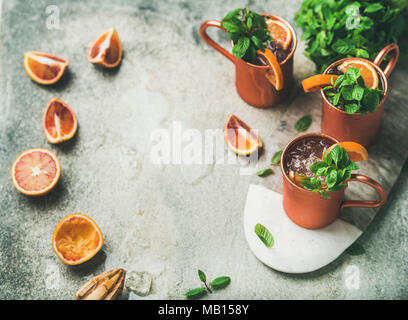Blutorange Moscow Mule Alkohol Cocktails mit frischen Minzeblättchen und friots und Eis in Kupfer Tassen an Bord über grauer Beton Hintergrund Kopie Raum Stockfoto