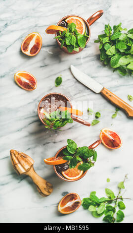 Flachbild-lay von Blutorange Moscow Mule Alkohol Cocktails mit frischer Minze und Eis in Kupfer Becher über weißem Marmor Hintergrund, Ansicht von oben, vertikale Zusammensetzung Stockfoto