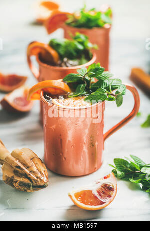 Blutorange Moscow Mule Alkohol Cocktails mit frischen Minzeblättchen und Eis in Kupfer Becher über weißem Marmor Hintergrund, selektiver Fokus Stockfoto