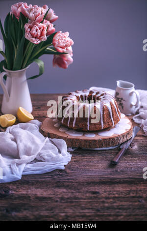 Bundt Cake mit Zitrone Glasur Nieselregen auf einem rustikalen Holztisch Stockfoto