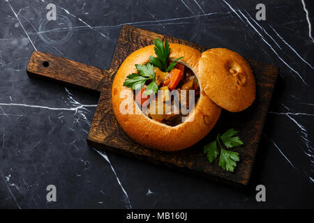 Rindfleisch Suppe Gulasch geschmort mit Kartoffeln, Karotten und Gewürze Brot auf schwarzem Marmor Hintergrund Stockfoto