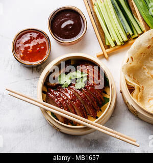 In Scheiben geschnitten Peking Ente in Bambus Steamer mit frischen Gurken serviert, grüne Zwiebeln, Koriander und gerösteten Wheaten chinesische Pfannkuchen mit Sauce Hoysin auf whit Stockfoto