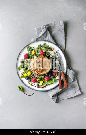 Vegan Kichererbsen Pfannkuchen in der Platte mit grünem Salat junge Rote Bete Blätter, Triebe, Beeren serviert, berry Sauce mit Tuch Serviette, Besteck über Graues con Stockfoto