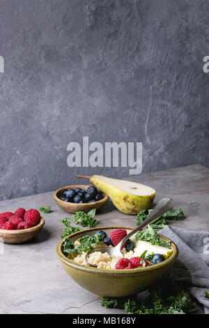 Vegan quinoa Porridge mit Grünkohl, Erdbeeren, Blaubeeren, in Scheiben geschnitten Birne, Honig auf Pendelarm in Keramik Schüssel mit Zutaten oben und Stoff Serviette über Stockfoto