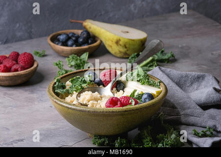 Vegan quinoa Porridge mit Grünkohl, Erdbeeren, Blaubeeren, in Scheiben geschnitten Birne, Honig auf Pendelarm in Keramik Schüssel mit Zutaten oben und Stoff Serviette über Stockfoto