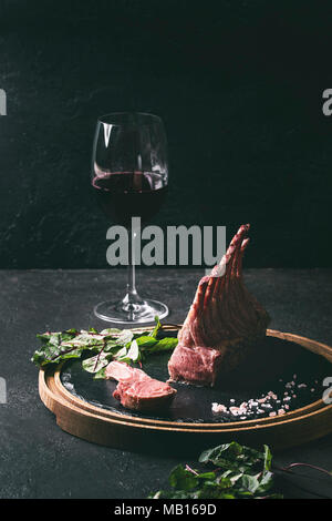 Gegrillter Lammrücken in Scheiben geschnitten mit Joghurt mint Sauce mit grünem Salat junge Rote Bete Blätter, Glas Rotwein, rosa Salz auf runden hölzernen Schiefer serviert b Stockfoto