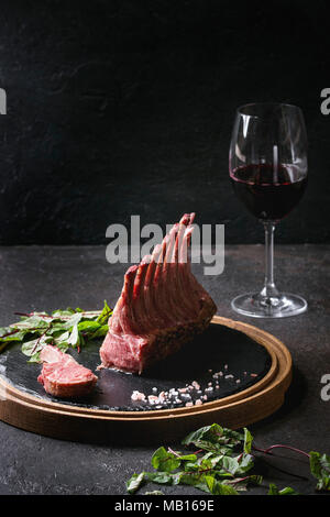 Gegrillter Lammrücken in Scheiben geschnitten mit Joghurt mint Sauce mit grünem Salat junge Rote Bete Blätter, Glas Rotwein, rosa Salz auf runden hölzernen Schiefer serviert b Stockfoto