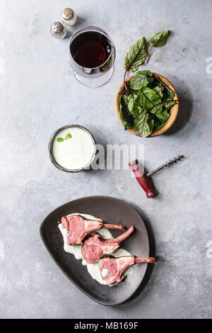 Gegrillter Lammrücken in Scheiben geschnitten mit Joghurt mint Sauce mit grünem Salat junge Rote Bete Blätter, Glas Rotwein, rosa Salz auf runden hölzernen Schiefer serviert b Stockfoto