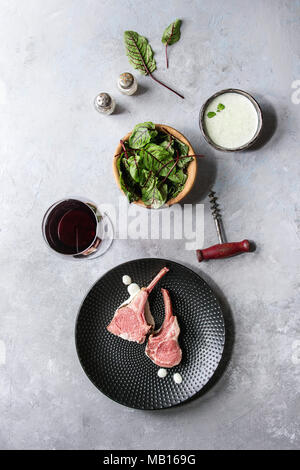 Gegrillter Lammrücken in Scheiben geschnitten mit Joghurt mint Sauce mit grünem Salat junge Rote Bete Blätter, Glas Rotwein, rosa Salz auf runden hölzernen Schiefer serviert b Stockfoto