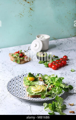 Vegetarische Sandwiches mit Avocado, Ricotta, Eigelb, Spinat, Tomaten auf Vollkorn Toast Brot auf Keramikteller mit Zutaten oben Ove Stockfoto