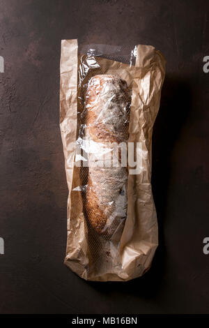 Laib des frisch gebackenen artisan Vollkorn ciabatta Brot in die Tasche über Dunkelbraun Textur Hintergrund. Ansicht von oben, kopieren. Stockfoto