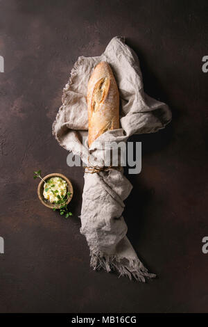 Laib des frisch gebackenen artisan Baguette im Leinen mit Butter und herbsover Dunkelbraun Textur Hintergrund. Ansicht von oben, kopieren. Stockfoto