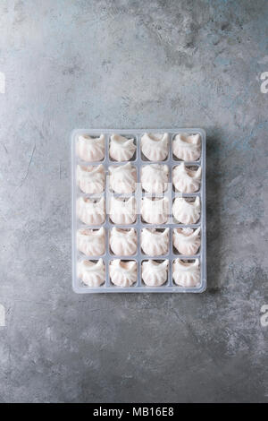 Tiefgekühlte Fertiggerichte asiatischen potstickers Klöße zu kochen von Garnelen in Kunststoffbox über grau Textur Hintergrund gefüllt. Ansicht von oben, Platz. Halbzeug Stockfoto
