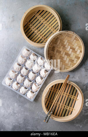 Tiefgekühlte Fertiggerichte asiatischen potstickers Klöße zu kochen von Garnelen in Kunststoffbox mit Stäbchen und Bambus Steamer über grau Textur Hintergrund gefüllt. Zu Stockfoto