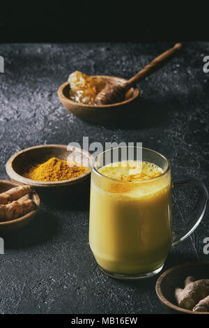 Tasse ayurvedischen Getränk golden Milch Latte mit Gelbwurz Kurkuma Pulver und Zutaten oben über schwarze Textur Hintergrund. Getonten Bild Stockfoto