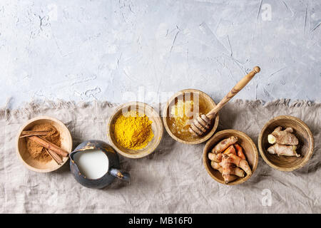 Zutaten für gelbwurz Latte. Boden Gelbwurz, curcuma root, Zimt, Ingwer, Bienenwaben in Holzschalen, Kanne Milch über grau Textur Hintergrund Stockfoto