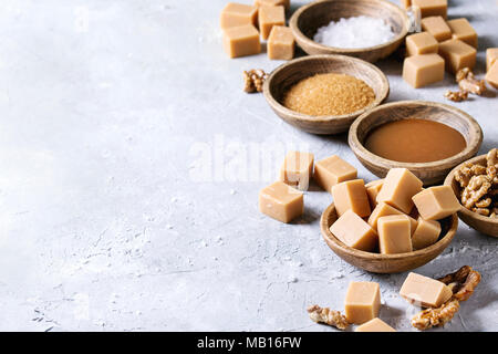 Gesalzene caramel fudge Bonbons mit Fleur de Sel, Karamell Sauce serviert, braunen Rohrzucker und karamellisierte Walnüsse in Holz Schalen über grau Textur backgroun Stockfoto