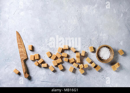 Gesalzene caramel fudge Bonbons mit Fleur de Sel in Houten und Messer über grau Textur Hintergrund serviert. Ansicht von oben, kopieren. Stockfoto