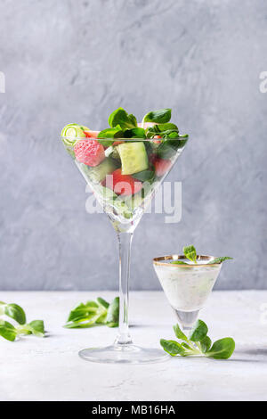 Frühling Sommer Diät Salat mit Erdbeeren, Gurken, grüne Feld Salat und Joghurt Minze Sauce cocktail Glas über grau Textur Hintergrund serviert. C Stockfoto