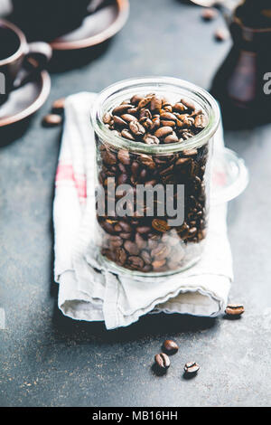 Kaffee Zusammensetzung auf dunklem Hintergrund. Kaffee Bohnen im Glas, Kaffeetassen und alten metallischen Kaffeemaschine Stockfoto