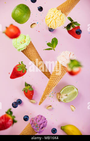Süß und bunt Eis in der Waffel Kegel mit Streuseln und Zutaten fallen oder Fliegen in Bewegung gegen Rosa shabby chic vintage Hintergrund Stockfoto