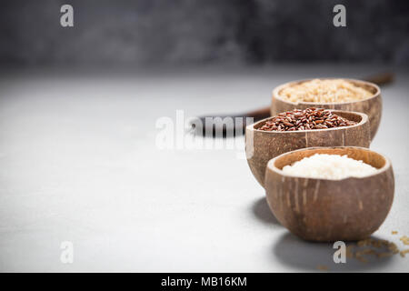 Sortiment von verschiedenen Reis in Schalen: Reis Berry, brauner Reis und Risotto Reis auf grauem Beton Hintergrund. Stockfoto