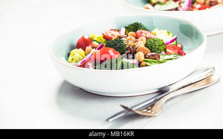 Gesund vegan Energie Steigerung der Salat mit Kichererbsen, Brokkoli, Tomaten, roten Zwiebeln, Spinat und Nüsse in blauen Platte auf konkreten Hintergrund, selektive fo Stockfoto