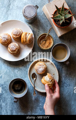 Weibliche Hand packte einen Choux au craquelin von der Platte. Stockfoto