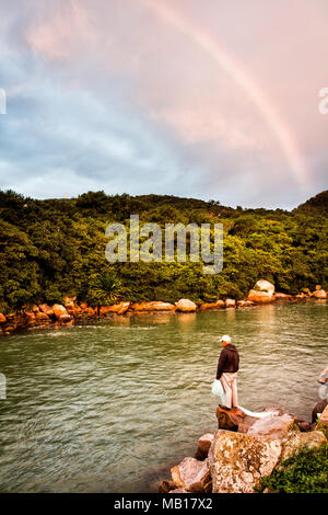 Mann, der auf einem Felsen am Kanal Barra da Lagoa steht. Florianopolis, Santa Catarina, Brasilien. Stockfoto