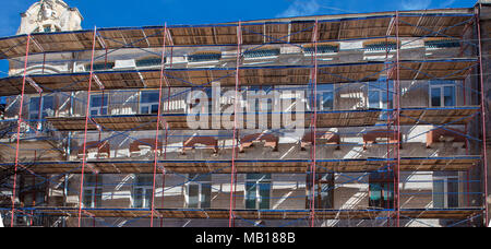 Gerüstbau in der Nähe ein Haus im Bau für externe Gipse, hohe Gebäude in der Stadt, weiße Wand und Fenster, gelbe Leitung Stockfoto