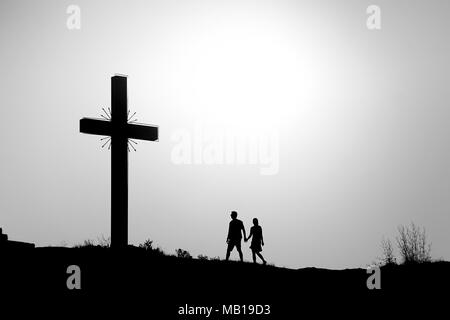 Silhouette von Kreuz auf Sonnenuntergang mit Mann und Frau halten sich an den Händen und vorbei an Stockfoto