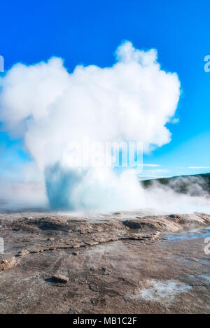 Dampf aus einem Geysir im Yellowstone, kargen Boden Dampf Wolken vor blauem Himmel. Stockfoto